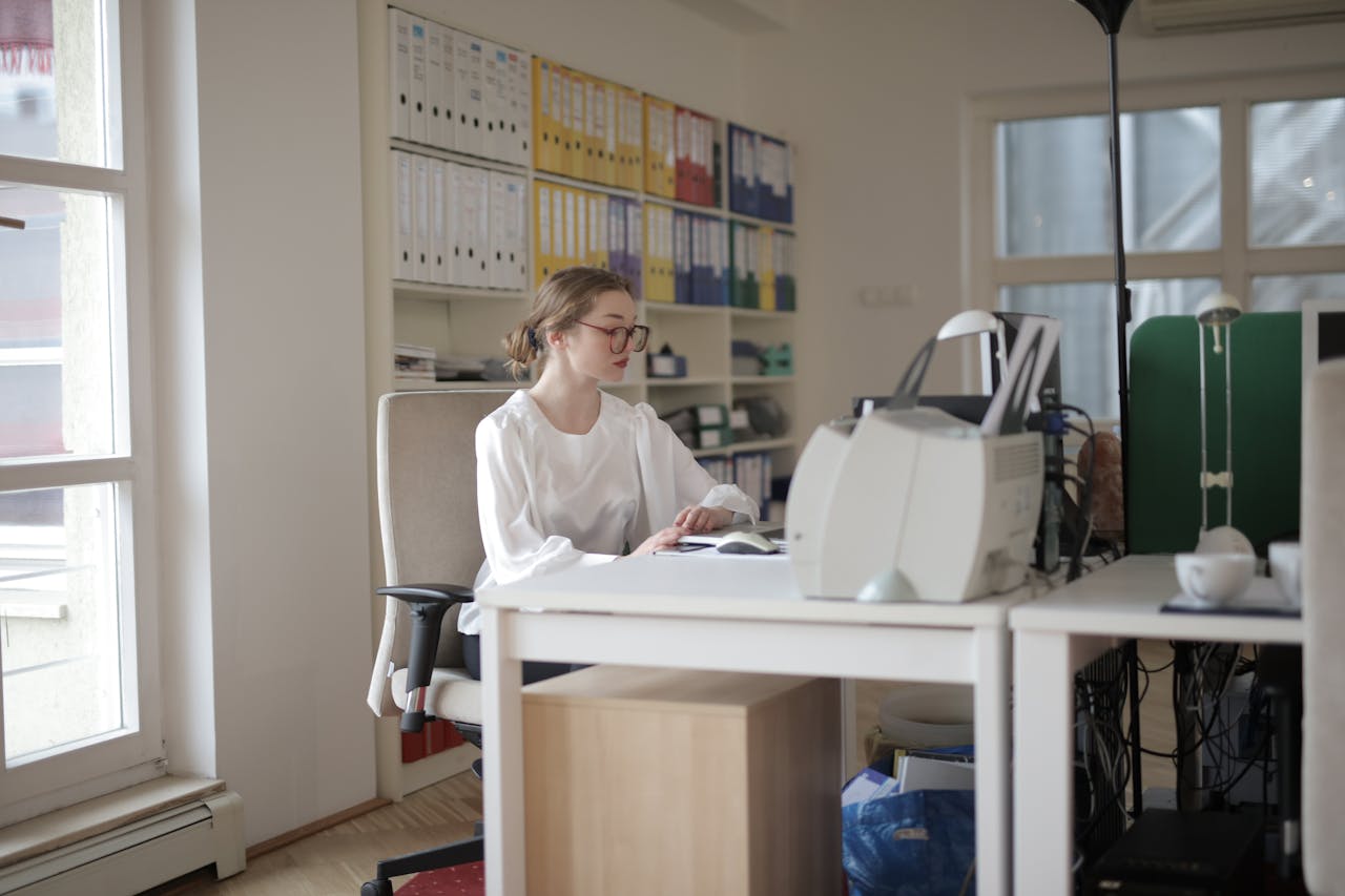 about-img Focused woman working in a modern office filled with files and equipment.