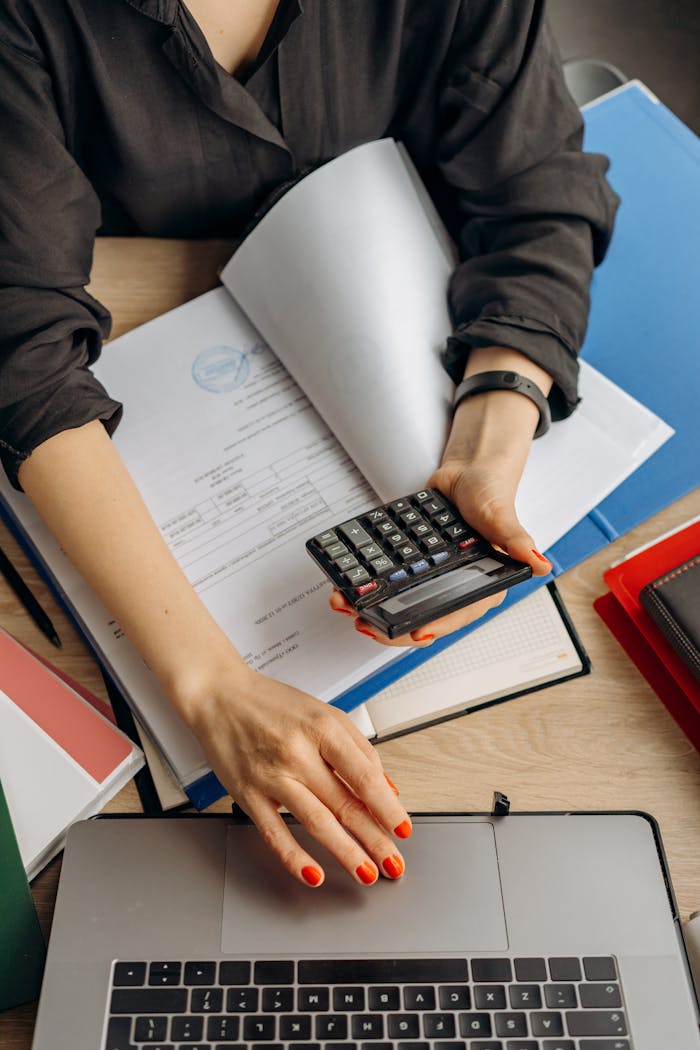 vision A business professional uses a calculator among documents and laptop on a desk for financial tasks.